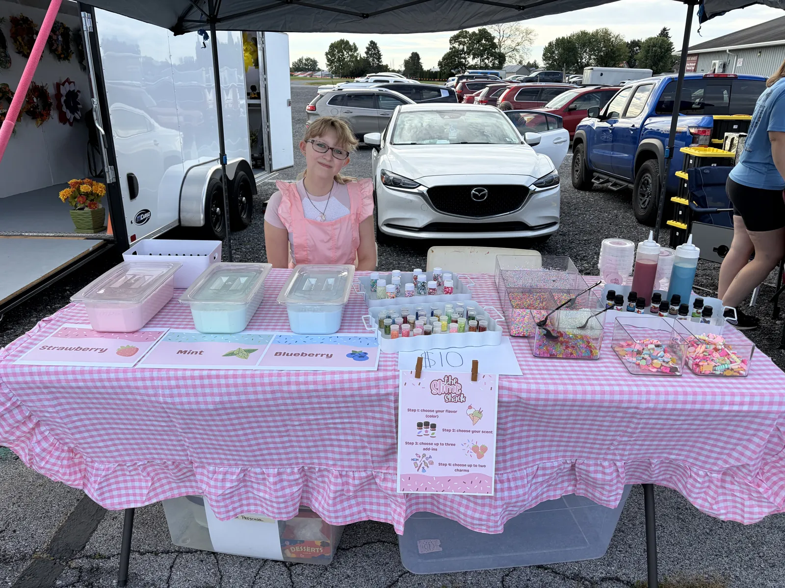 The Slime Shack stand with a pink gingham tablecloth, slime tubs, and toppings